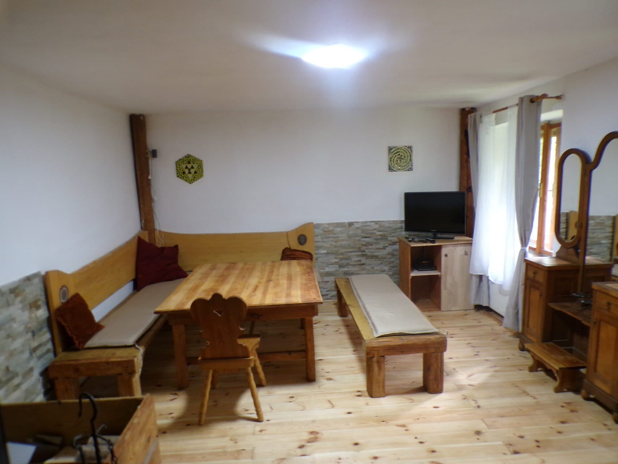 Obývací pokoj s rohovou dřevěnou lavicí, masivním stolem a televizí, podlaha z širokých prken